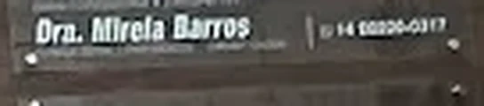 Detalhe ampliado da placa: “Dra. Mirela Barros” e o número de telefone, no painel da fachada.
